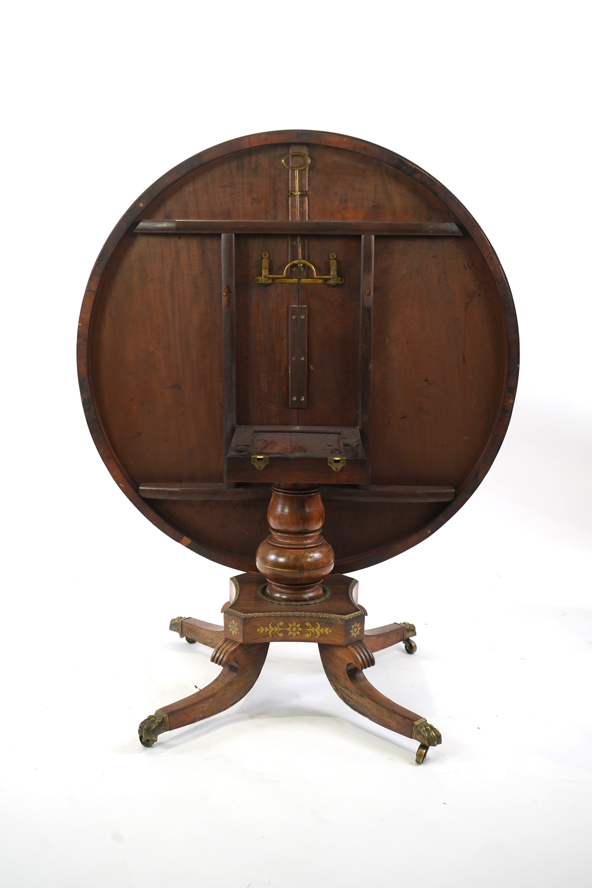 A Regency cut brass inlaid and gilt metal mounted circular rosewood breakfast table, the bird's-eye maple banded tilt top on baluster column, concave platform and quadruple downswept base with cast claw caps and castors,